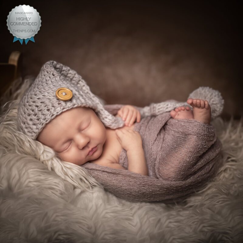 Photograph of sleeping newborn baby with grey sleeping hat and purple wrap.