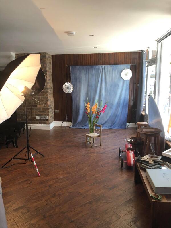 Behind the scenes photograph of Clare's studio showing various props, a blue backdrop and large umbrella light.