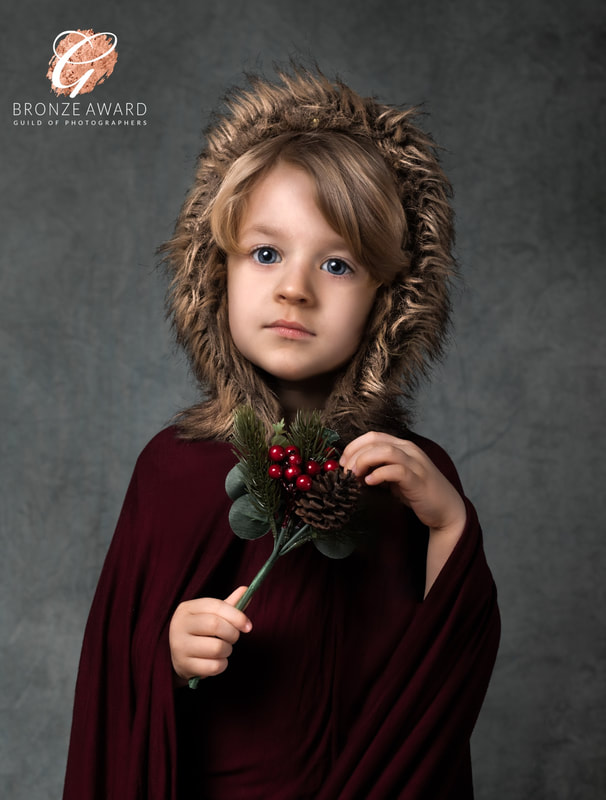 Young boy in burgundy cloak and fur hood holds holly.