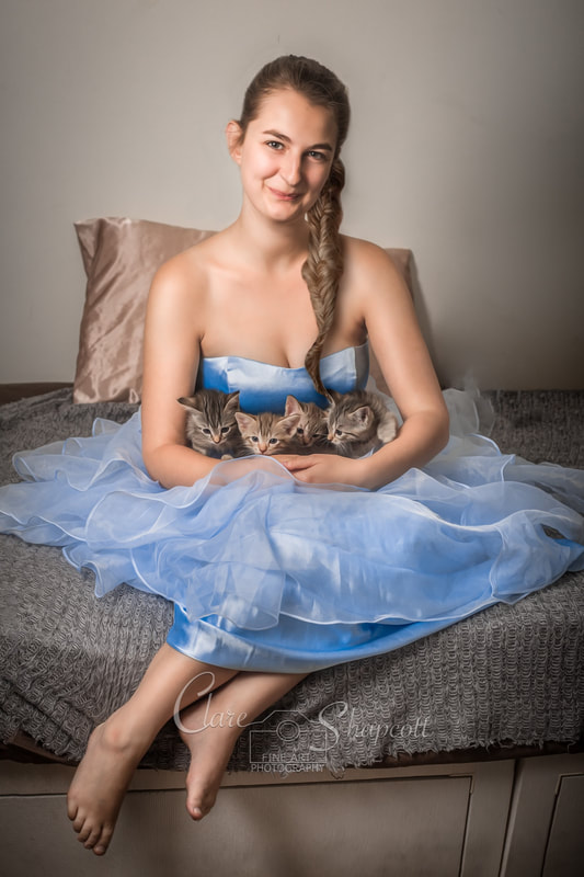 Young lady in light blue dress sits on floor as she cuddles four young brown kittens in her lap.