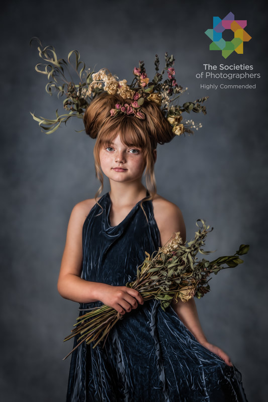 Fine art child portrait of girl in blue dress with dried flowers in hair holding bundle of flowers.
