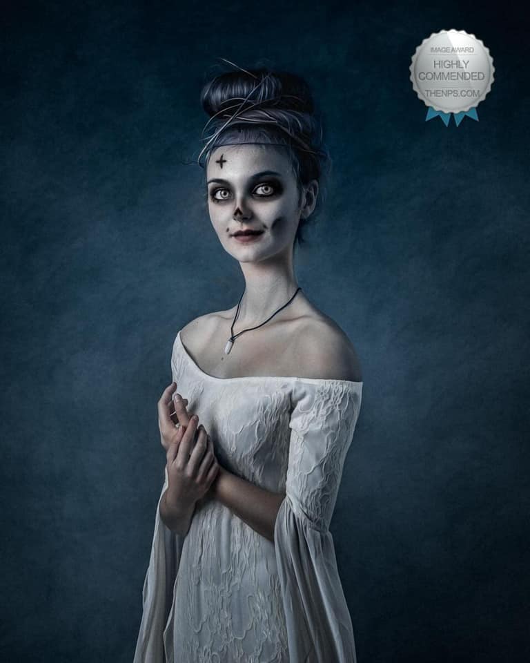 Young woman in white dress with skeleton themed make up poses with hands in front of stomach.