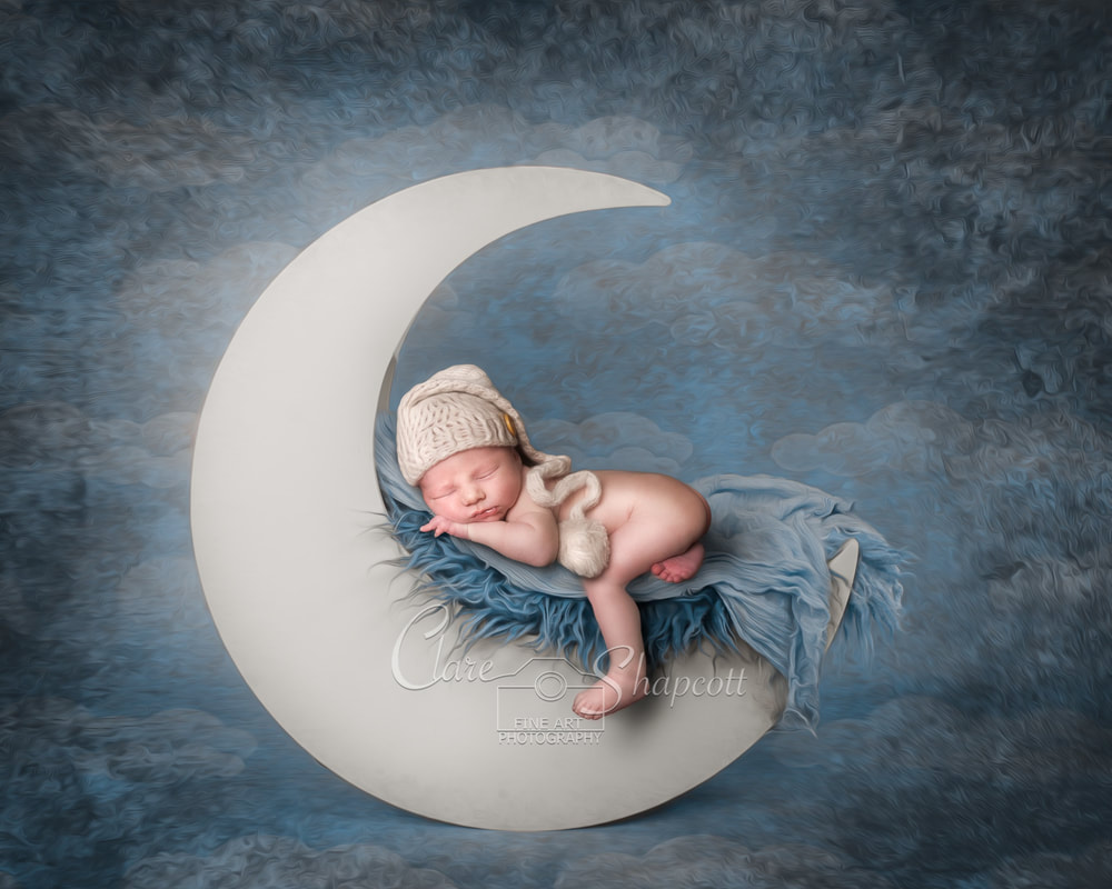 Professional newborn photoshoot of baby asleep on soft blue material on top of a white glowing moon.