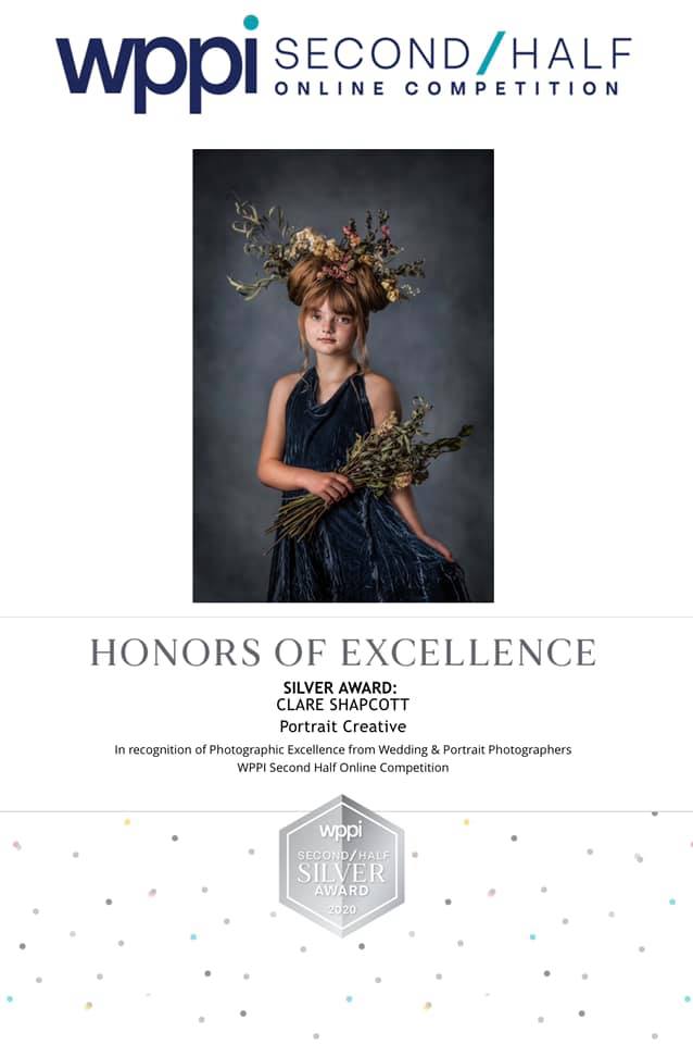 Award from the WPPI of a young girl in blue dress and flowers in her hair, holding a large bunch of dried flowers.