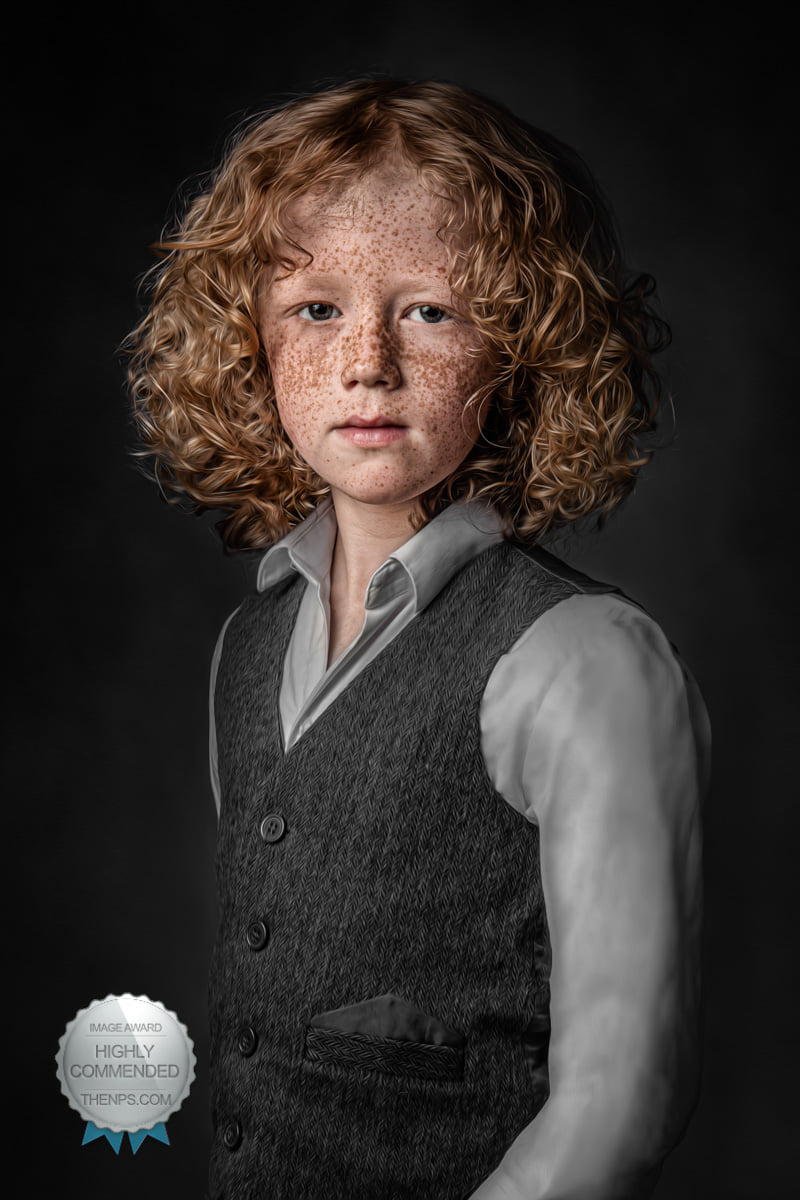 Young, freckled boy with curly blonde hair stands while wearing smart grey waistcoat and shirt.
