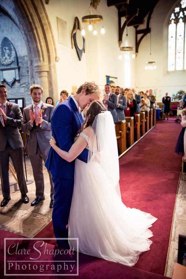 Groom in blue suit kisses bride at church on red carpet