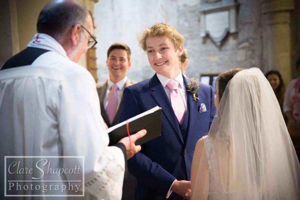 Very happy groom looks at priest while holding bride's hands