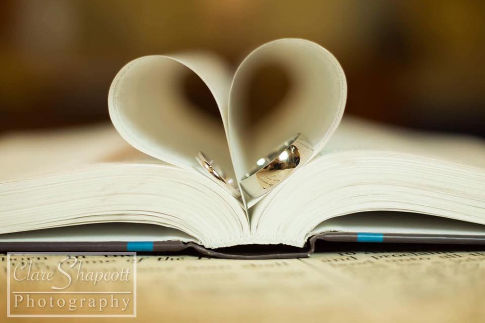 Close up photograph of wedding rings on book to fold pages into a 3D heart
