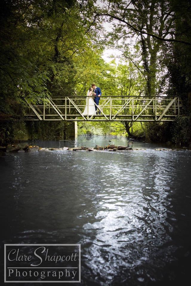 Wedding photoshoot newlyweds kissing each other on top of bridge over wide river near trees