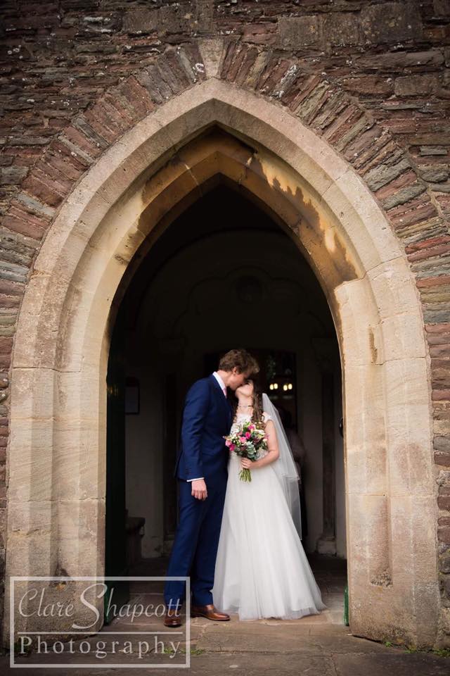 Clare Shapcott wedding photograph of newlyweds kissing under stone archway of church