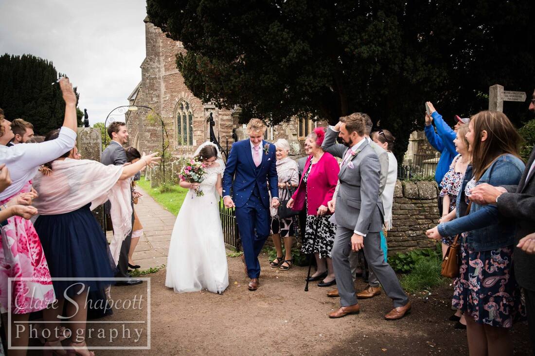 Guests throw confetti at bride and groom outside wearing blue suit