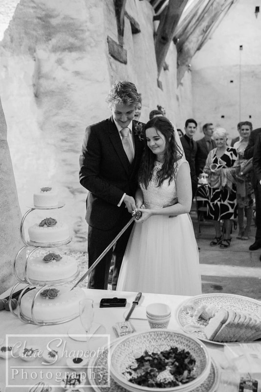 Black and white photograph of bride and groom cutting wedding cake with a sword