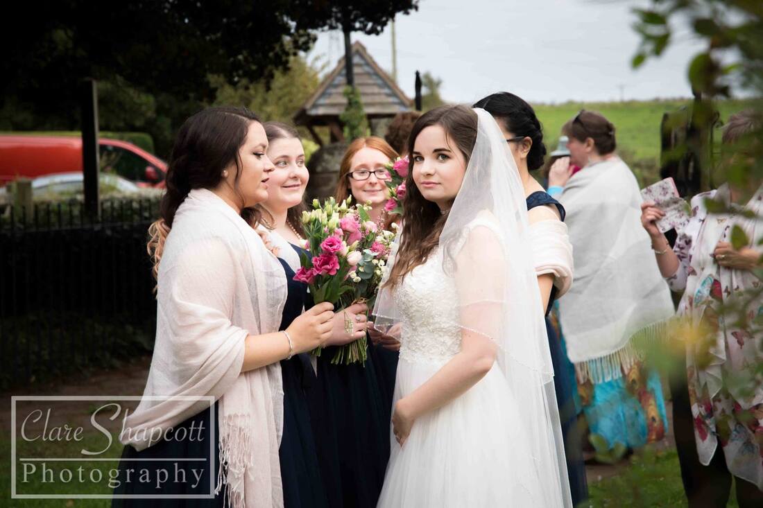 Bride looks at camera next to bridesmaids holding flowers