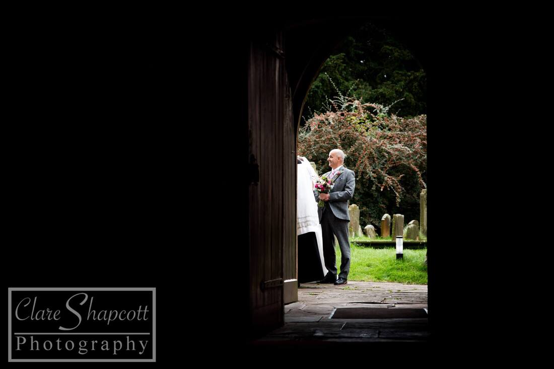 Father of bride waits outside church next to blossom tree from doorway