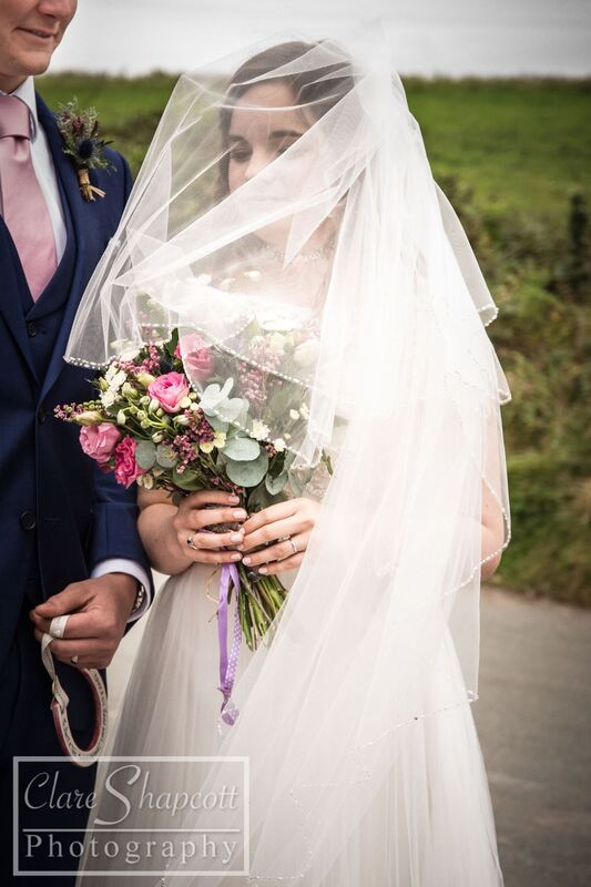 Bride's white veil blown over face while holding pink and white flowers