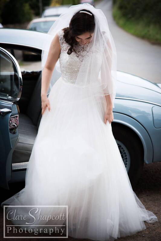 Professional wedding photograph of bride outside of car focusing on long, bold dress