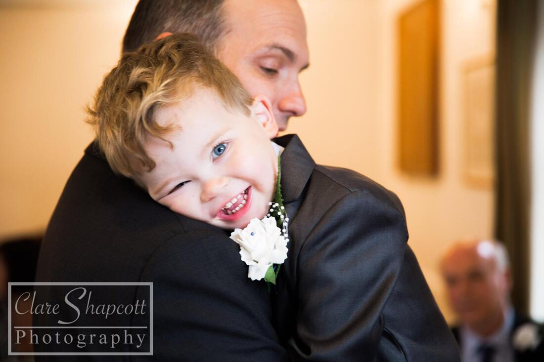 Son of groom hugging father and wearing white flower