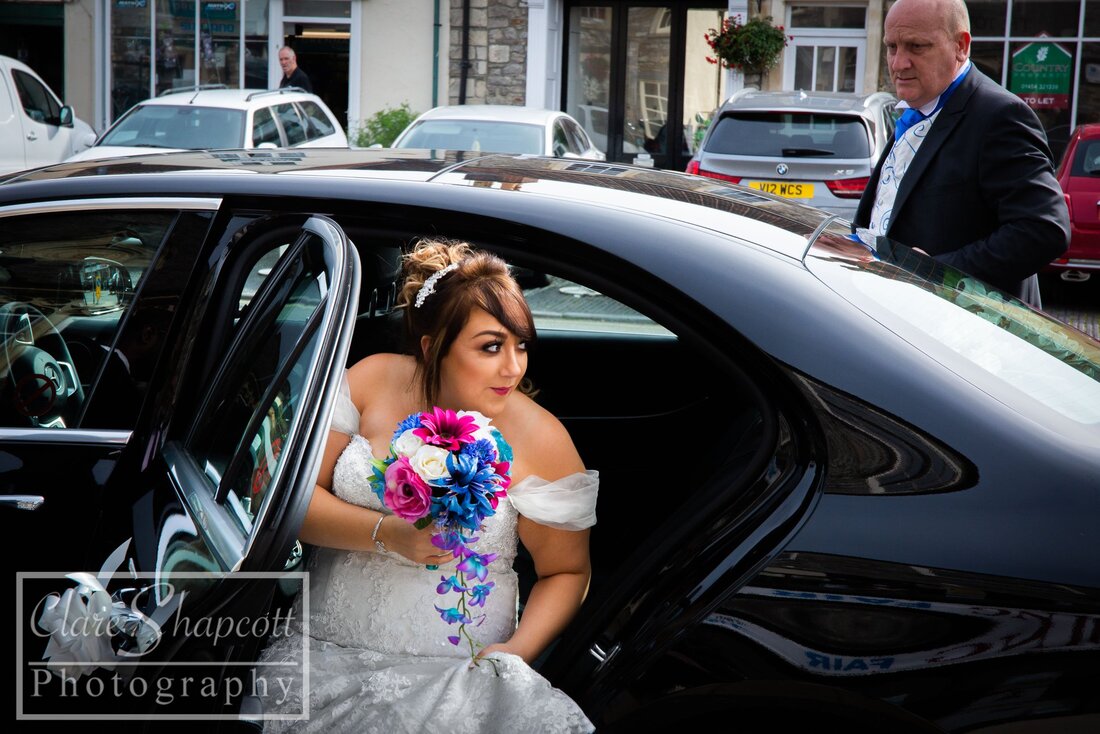 Bride holding pink and blue flowers while stepping out of black car