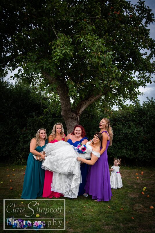 Bride's friends hold her for professional wedding photograph with child behind