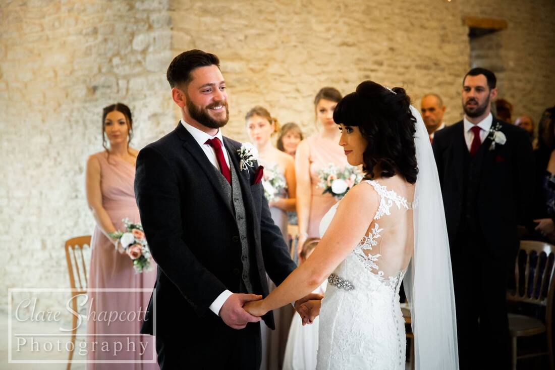 Happy groom holding bride's hands with guests in background and stone wall