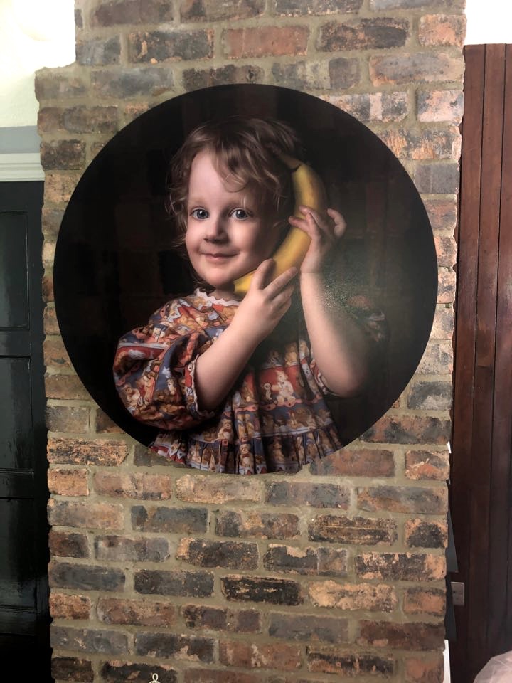 Circular fine art display of young girl in teddybear dress holding banana to ear.