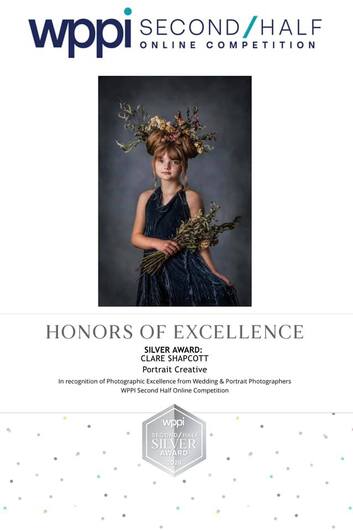 Honors of Excellence silver award photograph of girl in blue dress with flowers tied into her hair gracefully holding dried bundle of flowers.
