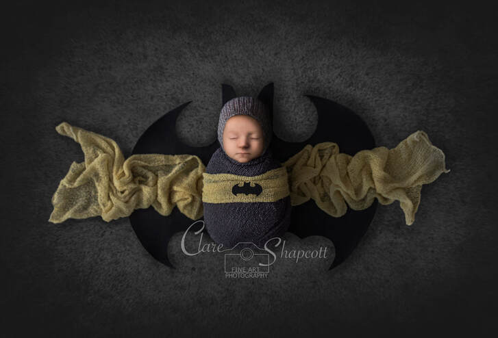Sleeping newborn with a batman themed wrap lies down on top of batman logo.