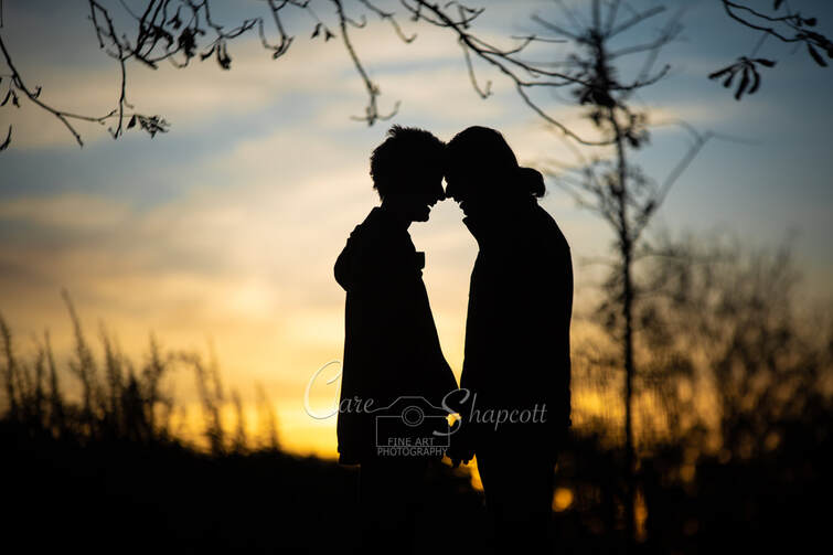 Silhouette of happy couple in front of sunset with black trees in background.