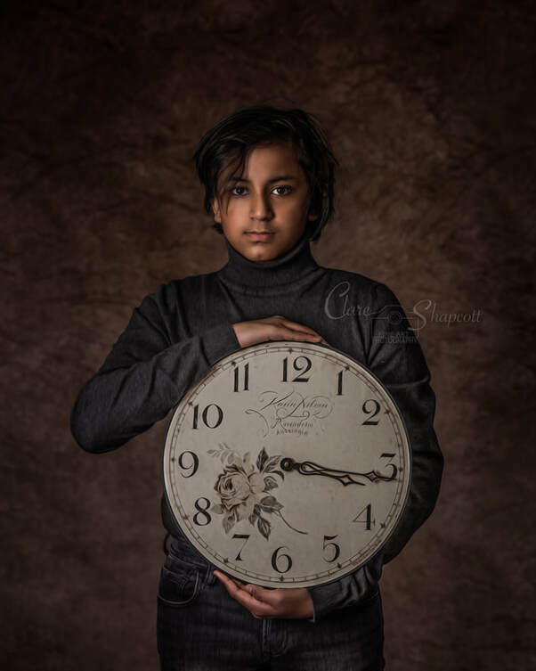 Boy in grey turtleneck faces camera as he holds a white clock with a flower pattern.