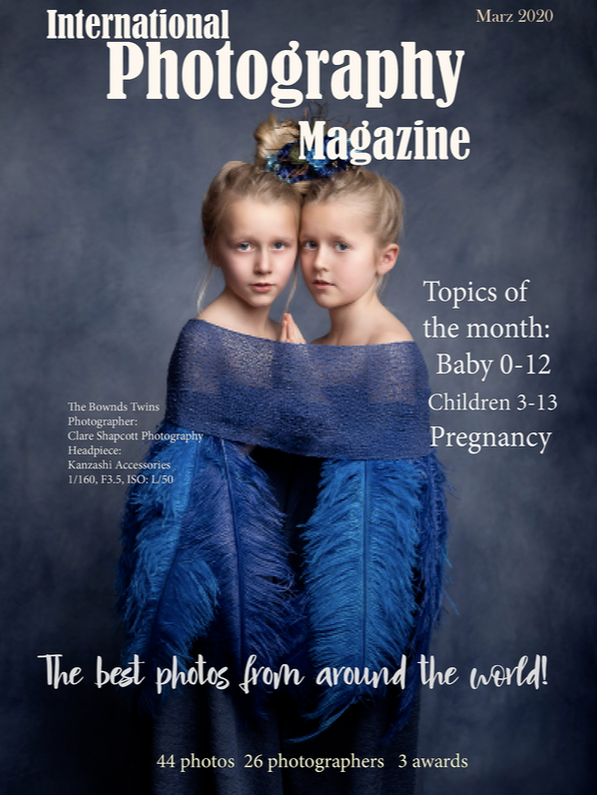 Front cover of International Photography Magazine showing a fine art portrait by Clare Shapcott of two girls surrounded by large blue feathers and blue wrap holding hands with each other.