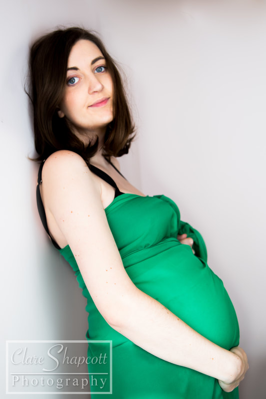 Beautiful woman leaning against white wall in green maternity dress