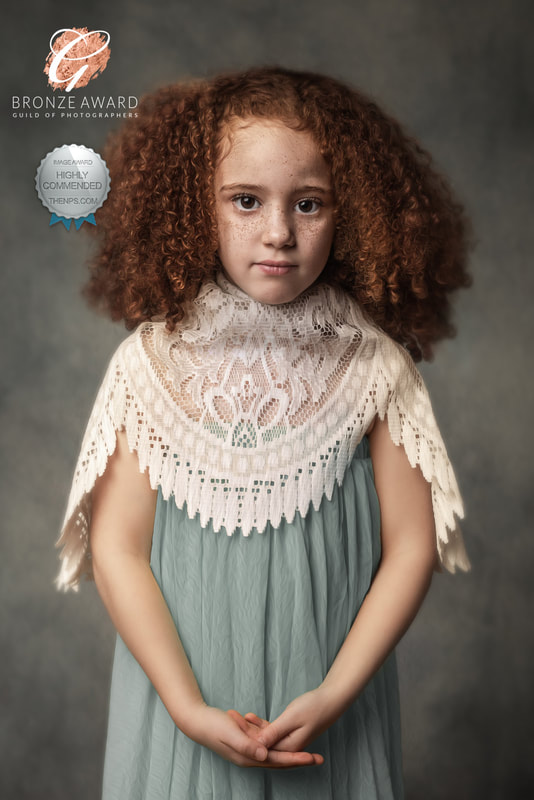 Multi award-winning photograph of young girl with curly red hair and freckles in green dress and white lace holding her hands together.