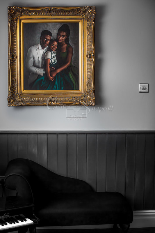 Fine art family portrait displayed in beautifully detailed gold frame on a wall above a black chaise sofa and toy piano.