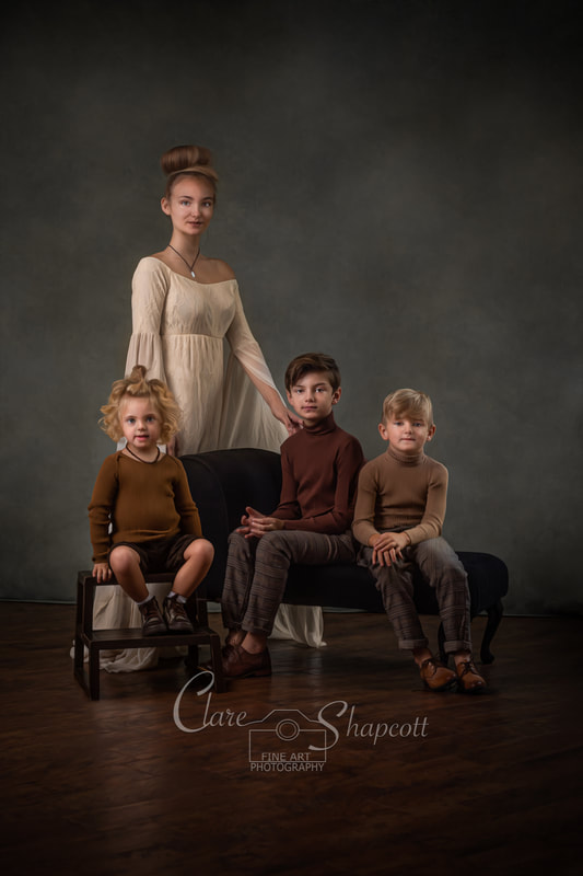 A group of four children of differing ages post on step ladder and black chaise couch wearing smart brown clothes.