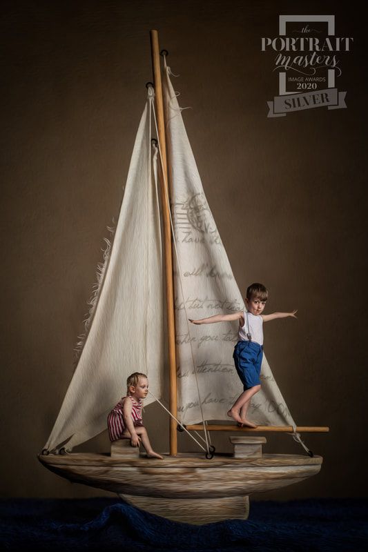 Two young children pose on miniature wooden boat in creative fine art portrait.