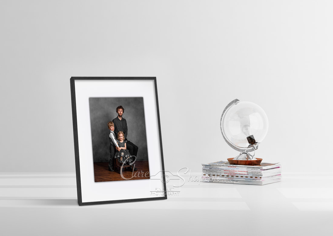 Picture frame showing a father with his son and daughter, displayed in a white room next to a globe shaped lamp.
