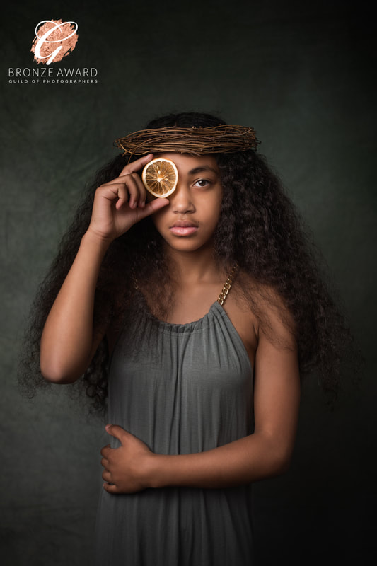 Photograph of teenage girl with long black curly hair in green dress holding dried orange slice in front of her eye.