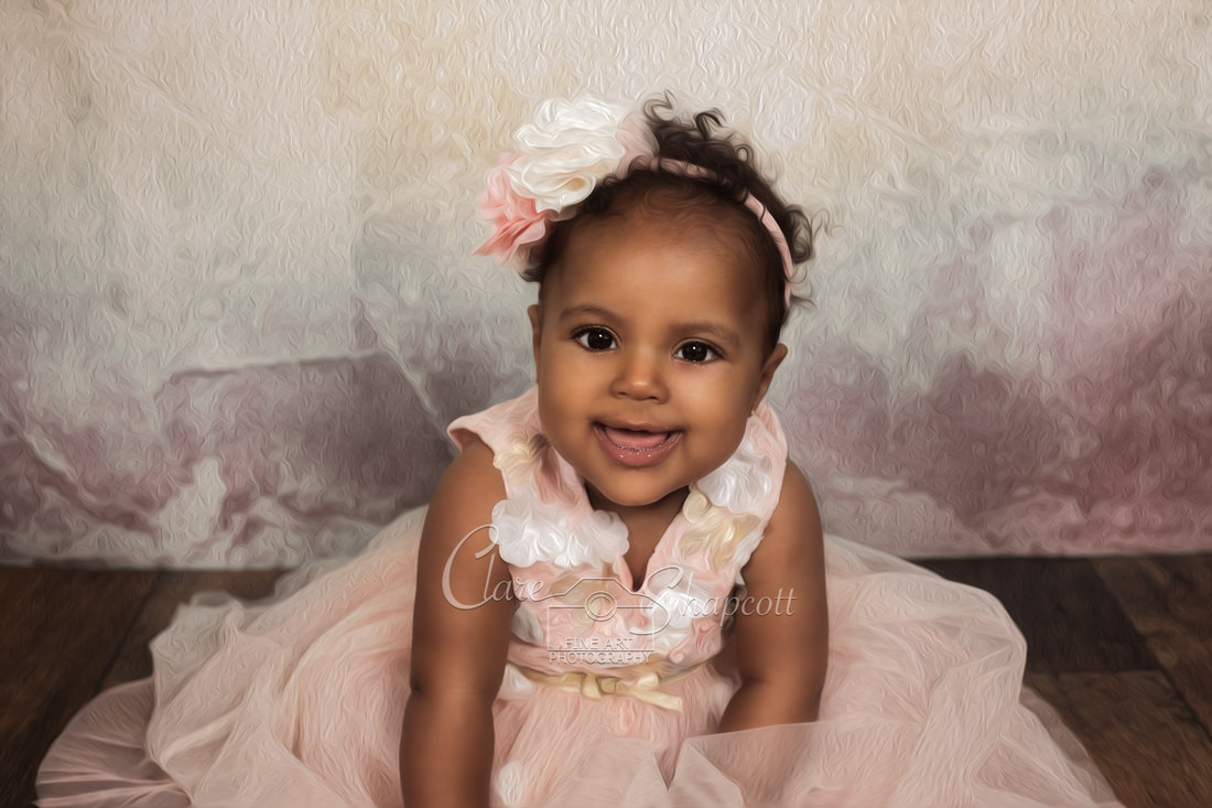 Smiling baby sits up in pink dress with white and pink flower headband and smiles at camera.