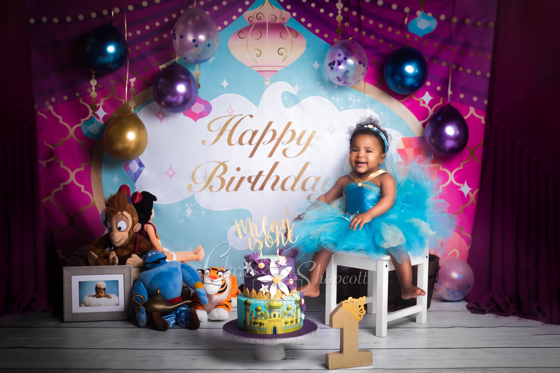 Cake smash photoshoot with Aladdin themed toys and background, with purple, blue and gold balloons.