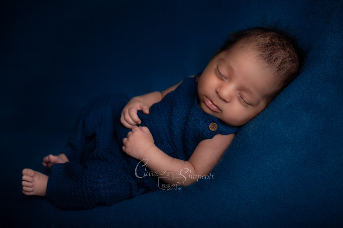 Bristol studio photograph of sleeping newborn baby in blue clothes on top of soft blue material.