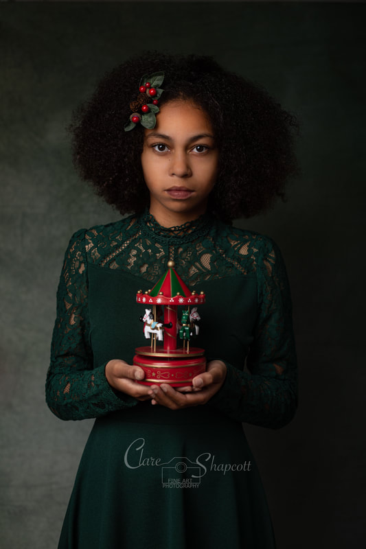 Teenage girl poses in front of camera with Christmas carousel music player with green dress and holly hair accessory.